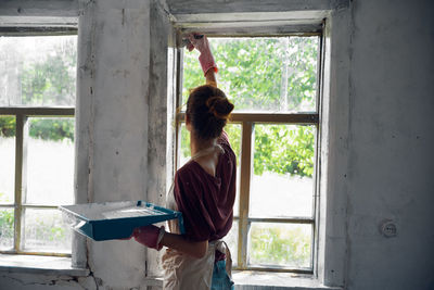 Rear view of woman painting window