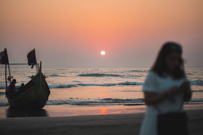 Rear view of woman standing at beach during sunset