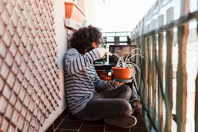 Side view of man holding potted plant while sitting in balcony