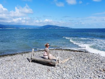 Girl sitting on shore at beach against sky