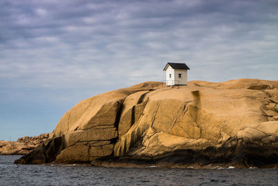 House on rock formation against cloudy sky