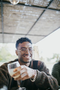 Portrait of smiling young man sitting with drink at patio during dinner party