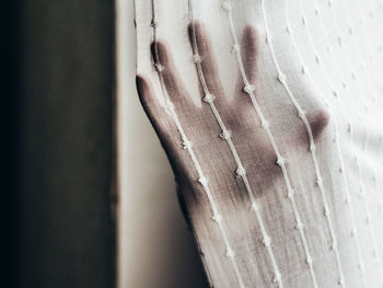 Cropped hand of person behind curtain at home