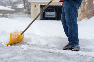 Low section of man cleaning snow on road