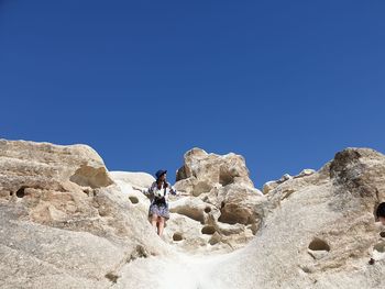 Low angle view of woman standing on rock against sky