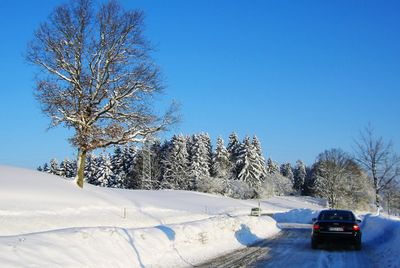 Snow covered road by trees against clear blue sky