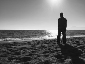 Rear view of silhouette man standing on beach against clear sky