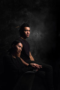 Portrait of young couple sitting against black background