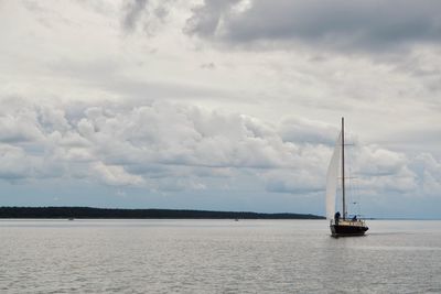 Sailboat sailing on sea against cloudy sky