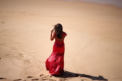 Rear view of woman in red gown walking on sand at beach