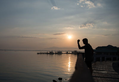 Silhouette man gesturing while standing by river during sunset