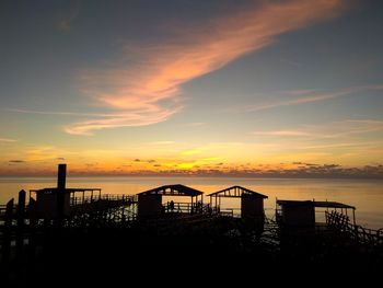 Silhouette built structure on beach against sky during sunset