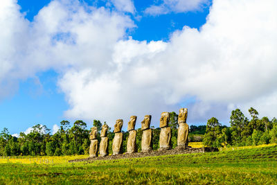 Moai statues on field against cloudy sky