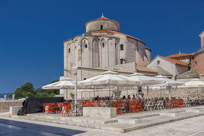 People at sidewalk cafe by church of st donatus against clear blue sky