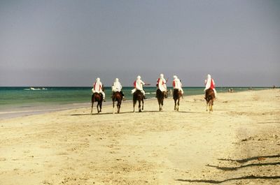 Rear view of men riding horses at beach