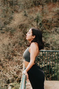 Side view of young woman standing against plants