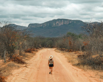 Unidentified tourist walking along a rural road with serra de bom sucesso in the background, bahia,