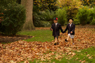 Full length of cute girl and boy walking on grass and leaves