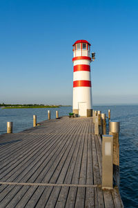 Lighthouse on pier by sea against clear sky