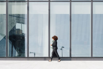 Businesswoman holding bag walking by glass wall