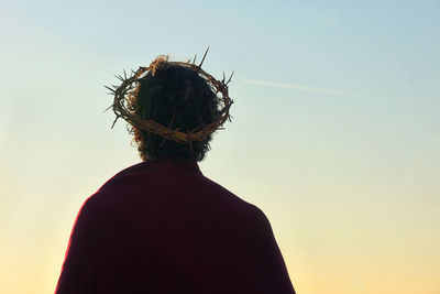 Rear view of man wearing wreath of thorns against sky