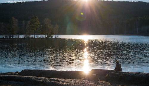 Silhouette man standing by lake against sky during sunset