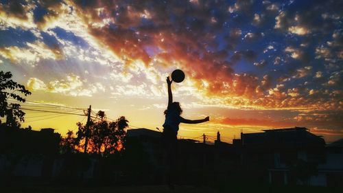 Girl playing basketball against sky during sunset