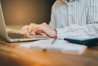 Midsection of businesswoman using laptop on table