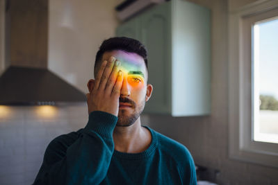 Rainbow light hitting face of young man covering one eye with hand