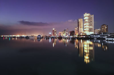 Illuminated buildings by sea against sky at night