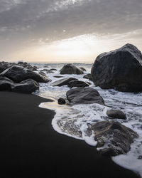 Rocks on beach against sky during sunset