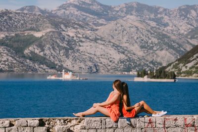 Woman sitting on swimming pool by lake against mountains