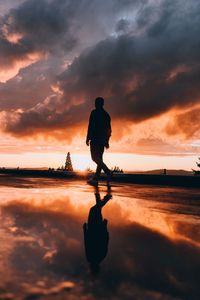 Silhouette man sitting by sea against sky during sunset