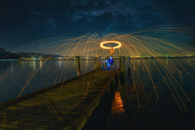 Man sitting on pier under wire wool at night