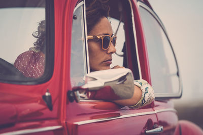 Mature woman wearing sunglasses looking through window while sitting in car