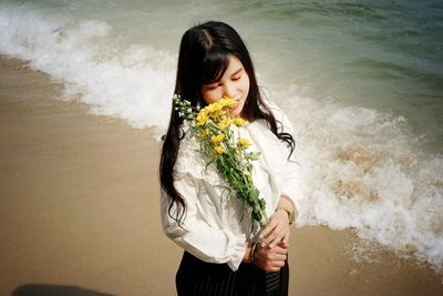 Woman holding flowers while standing at beach