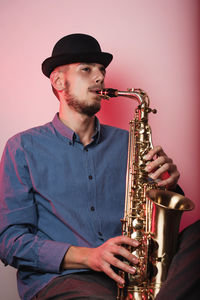 Young man wearing hat playing saxophone while sitting against wall