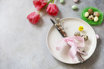 Festive easter table setting with painted eggs, spring flowers and cutlery on light grey tabletop. 