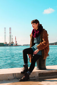 Thoughtful woman sitting at riverbank against sky