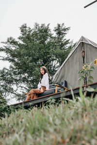 Young woman sitting on grass against trees