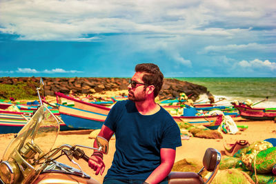 Indian man sitting on a motorbike at beach against sky