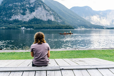 Rear view of man sitting on wooden bench near lake