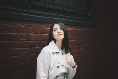 Woman looking away while standing by brick wall