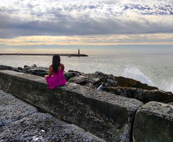 Woman sitting on rock by sea against sky