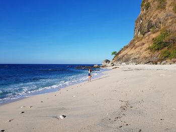 People walking on beach against clear blue sky