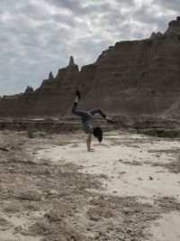 Full length of girl doing handstand on sand against sky