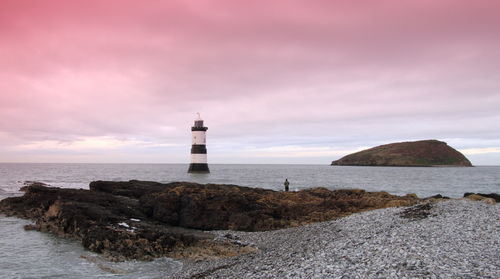 Black point lighthouse in sea at anglesey against cloudy sky during sunset