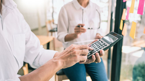 Midsection of woman using calculator by colleague in office