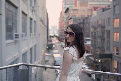 Portrait of young woman standing by railing in city