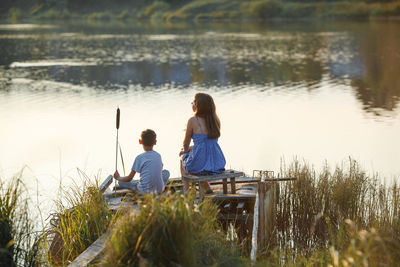 Rear view of friends sitting by lake